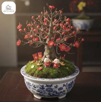 Cây mai đỏ bonsai mini trồng trong chậu sứ xanh trắng, trang trí tượng thần tài và phụ kiện Tết.